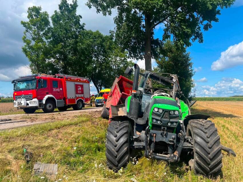 Osobne: rozbity ciągnik rolniczy z rozrzutnikiem przy drzewie, obok wóz strażacki i karetka
