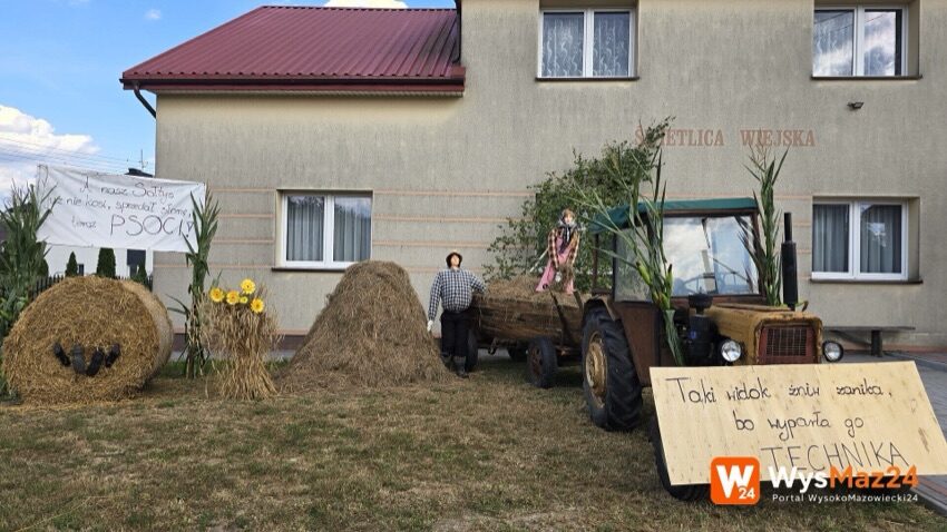 Jabłoń-Śliwowo: dożynkowa ozdoba wsi przed świetlicą - ciągnik z wozem, kopa siana i transparent o sołtysie
