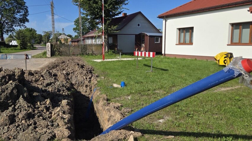 Wykop z nową niebieską rurą wodociągową przy zabudowaniach w Piętkach-Gręzkach