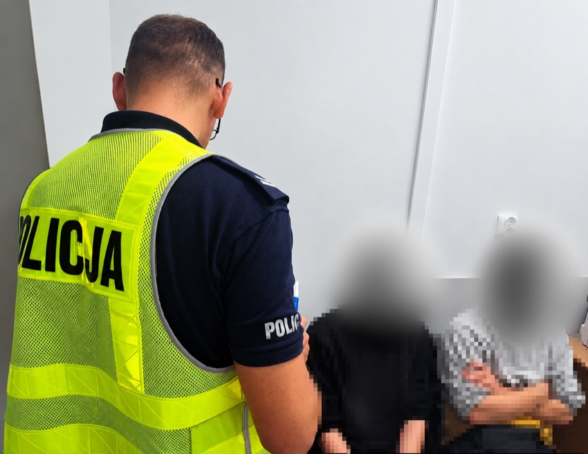 Policjant w kamizelce odblaskowej podczas kontroli, w tle dwaj mężczyźni z zamazanymi twarzami