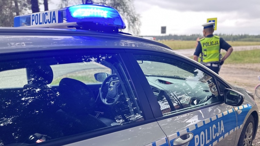 Radiowóz policyjny z włączonym sygnałem świetlnym, obok policjant - zdjęcie ilustracyjne