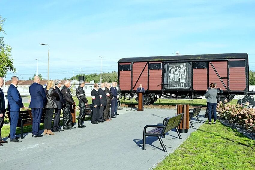 Wagon towarowy ustawiony na torach jako pomnik Sybiraków w Szepietowie, obok grupa uczestników uroczystości
