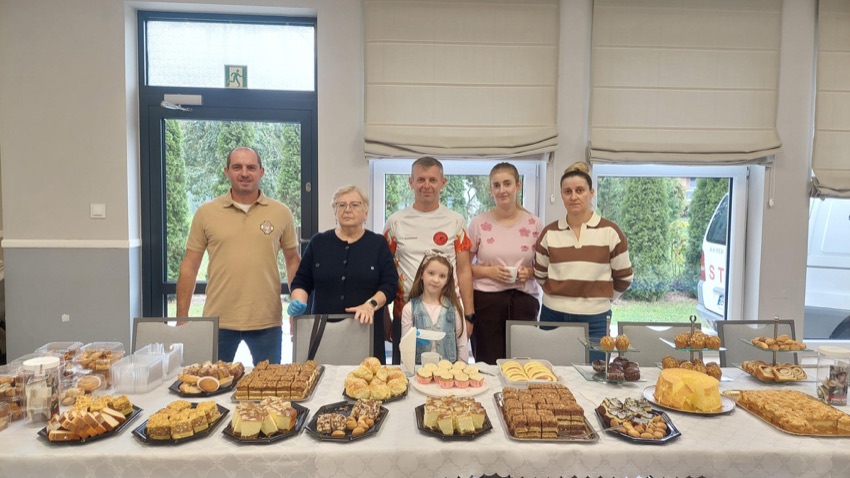 Strażacy z OSP Czyżew i wolontariusze przy stole z ciastami na kiermaszu dla Ignasia w Świetlicy Miejskiej