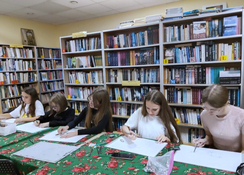 Młodzież rysuje przy stole na zajęciach rysunku i malarstwa w GOK w Nowych Piekutach