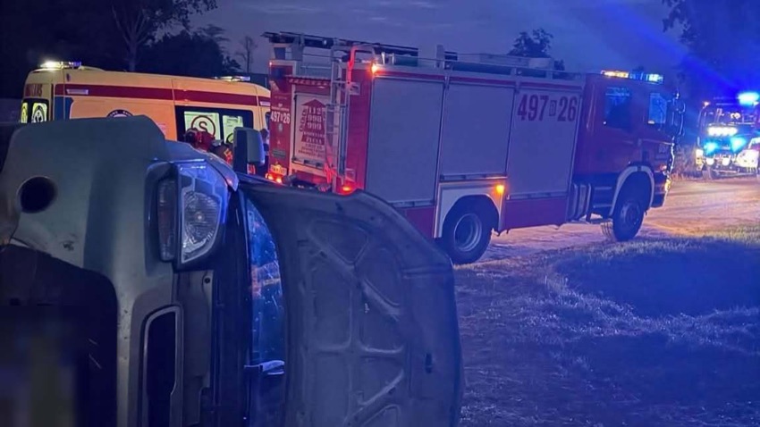 Samochód osobowy leżący na boku poza jezdnią w Rosochatem Nartołtach, w tle wóz strażacki i karetka