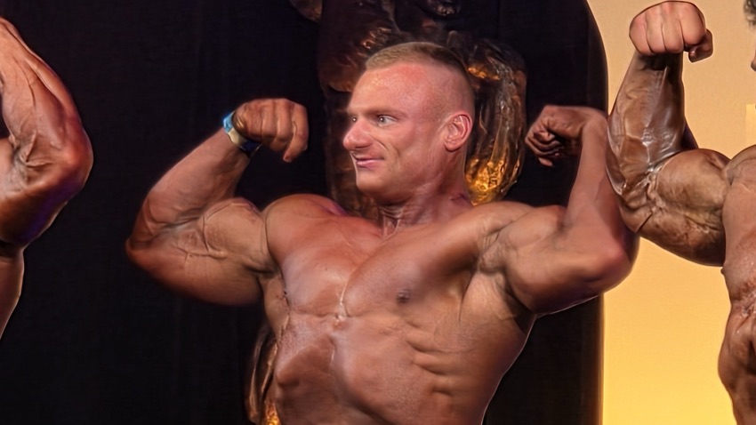Krystian Płoński w pozie podwójnego bicepsa na scenie zawodów NPC Grand Prix
