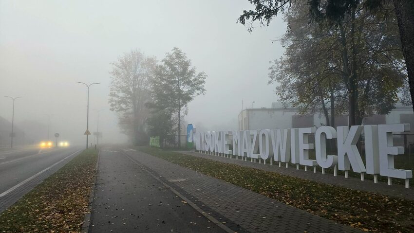 Wysokie Mazowieckie: gęsta mgła przy napisie z nazwą miasta, samochody jadą na włączonych światłach